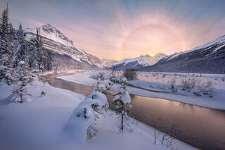 A sun halo overlooks a beautiful mountain, river, and snowy winter scene in the Canadian Rockies.  