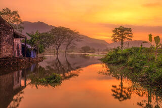 Remarkable sunset in fishing village in Java, Indonesia with man, house, lush green vegetation on water